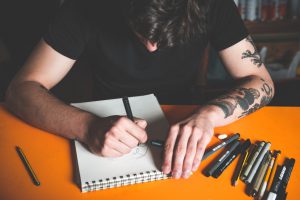Young tattoo artist draw a new sketch on paper before tattooing on skin