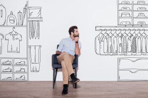 Young handsome man keeping hand on chin and looking away while sitting in the chair against illustration of closet in the background